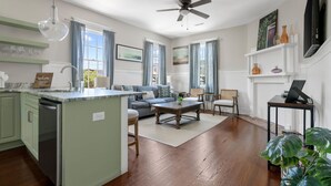 A modern kitchen with a central island, a dining area with a sofa, and a living room with a fireplace. - The Jasmine Suite | 3 Bedrooms Steps from Upper King (Charleston)