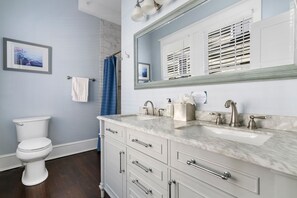 A bathroom with a toilet, a sink with a mirror, and a shower curtain. - The Pearl Suite | Chef's Kitchen | Sleeps 6 (Charleston)