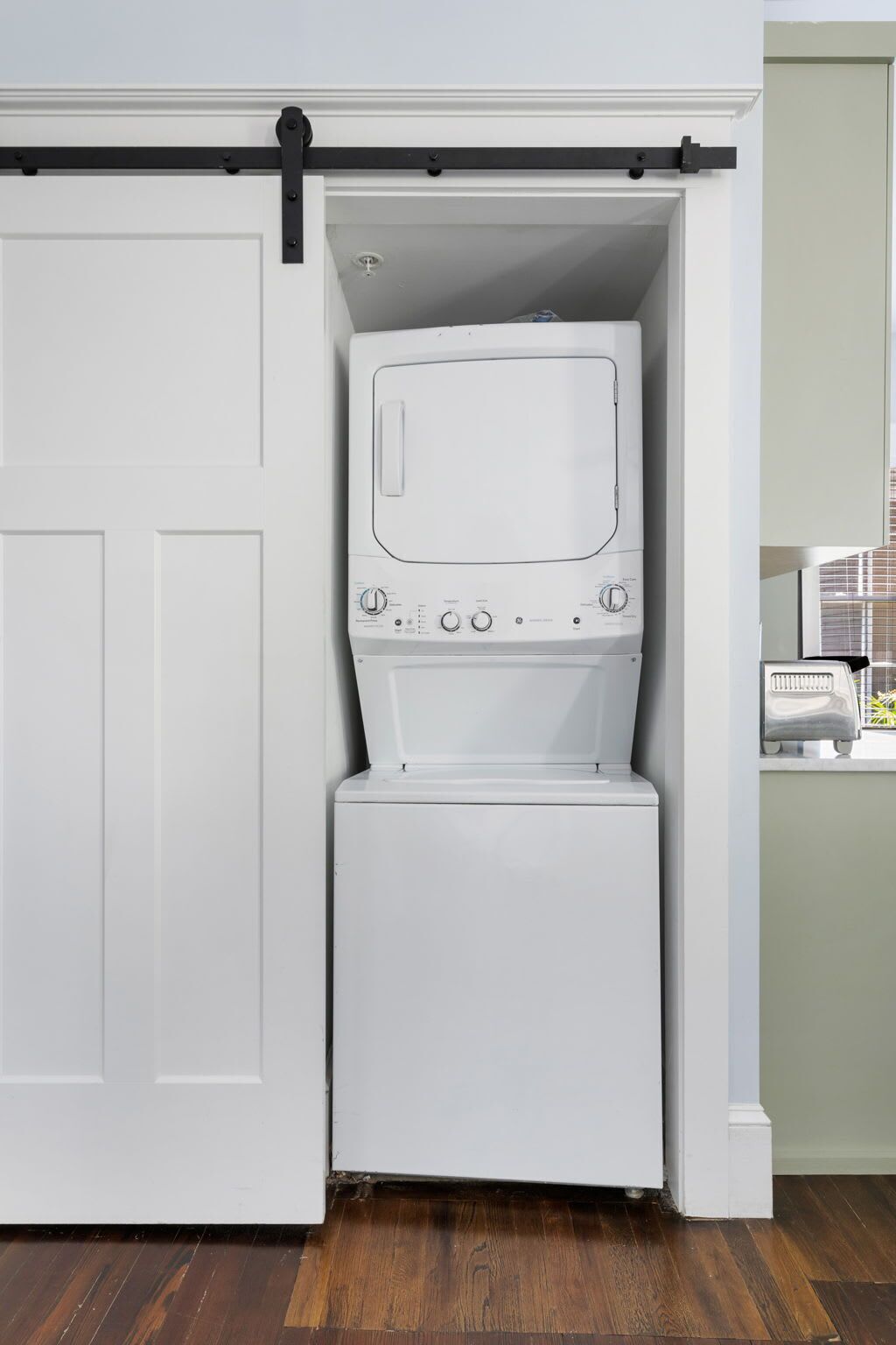 A compact laundry room with a front-loading washer and dryer, a sliding door, and a small window.