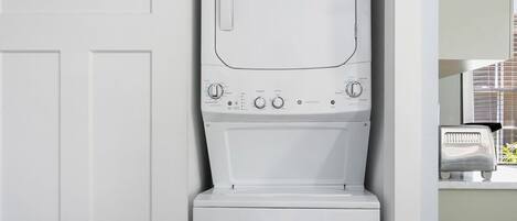 A compact laundry room with a front-loading washer and dryer, a sliding door, and a small window.