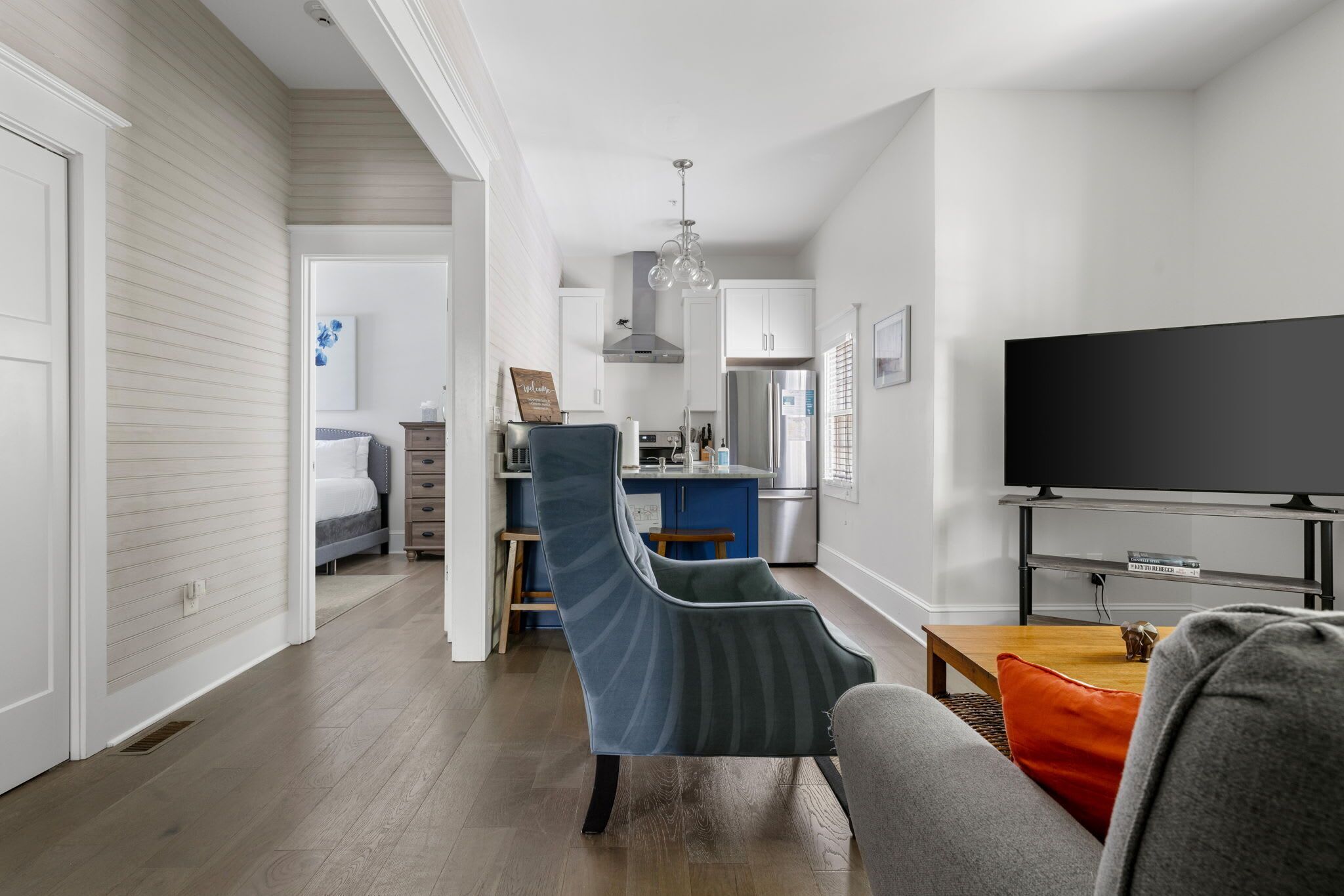 A modern living room with a sofa, a television, and a kitchen in the background.