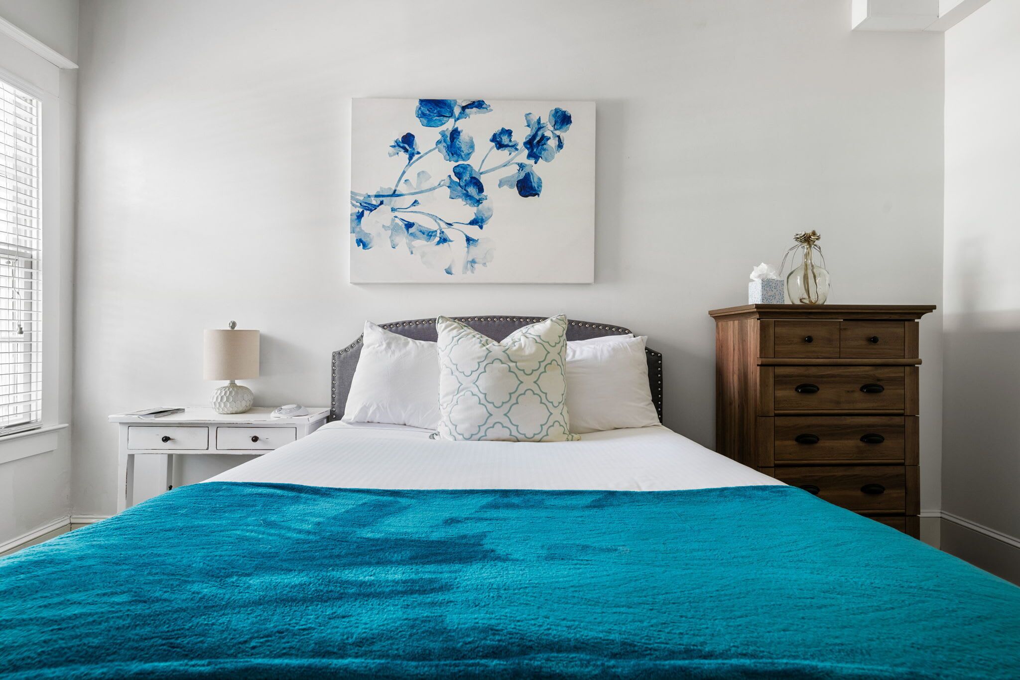 A bedroom with a bed, a nightstand, a dresser, and a wall-mounted painting.