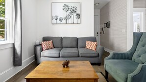 A living room with a grey sofa, a wooden coffee table, and a blue armchair. - The Oyster Suite | Walk to King + Cannon Green (Charleston)