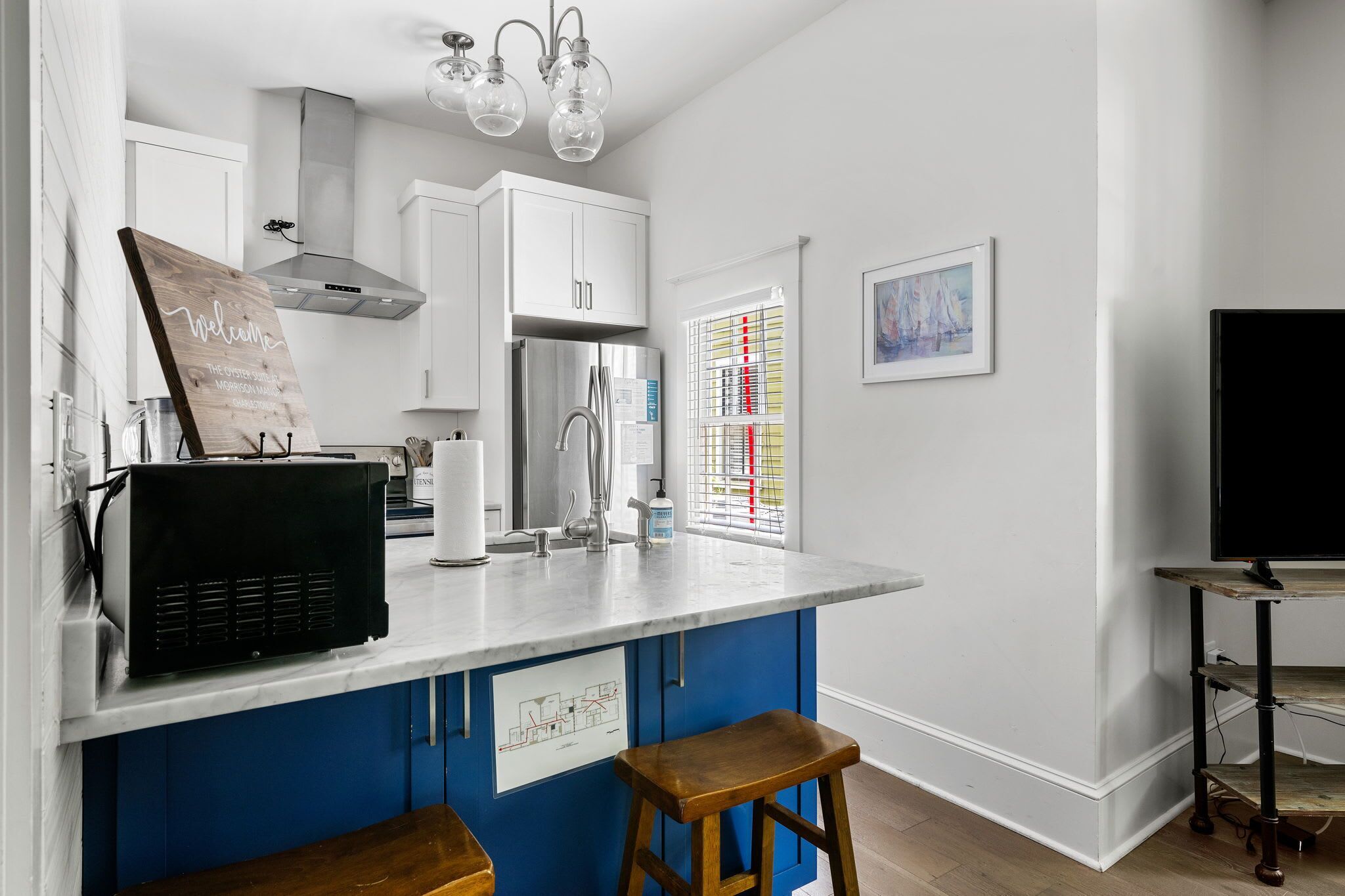 A modern kitchen with white cabinets, a stainless steel refrigerator, and a blue island with stools.