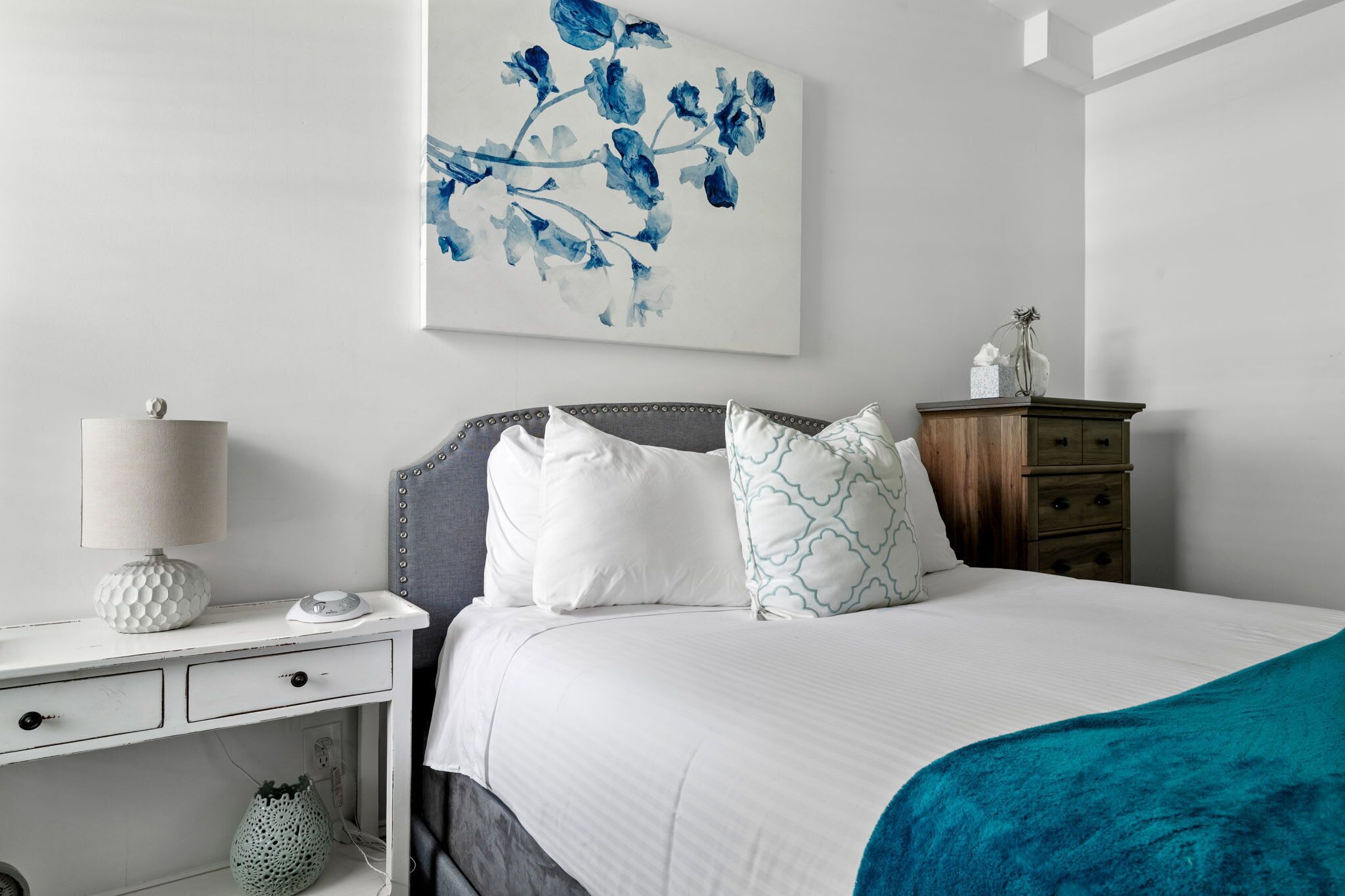 A neatly arranged bedroom with a bed, bedside table, lamp, and a wall-mounted artwork.