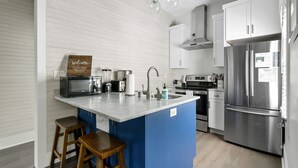 A modern kitchen with a central island, stainless steel appliances, and a blue accent wall. - The Oyster Suite | Walk to King + Cannon Green (Charleston)
