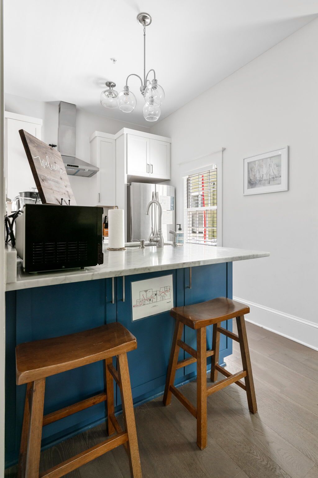 Eine moderne Küche mit blauer Akzentwand, weißen Schränken, einem Edelstahlkühlschrank und einem Holzhocker.
