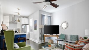 A modern living room with a green armchair, a glass coffee table, and a sofa with patterned cushions. A flat-screen TV is on a wooden stand. - The Hydrangea Suite | 3BR/2BA | Sleeps 6 (Charleston)