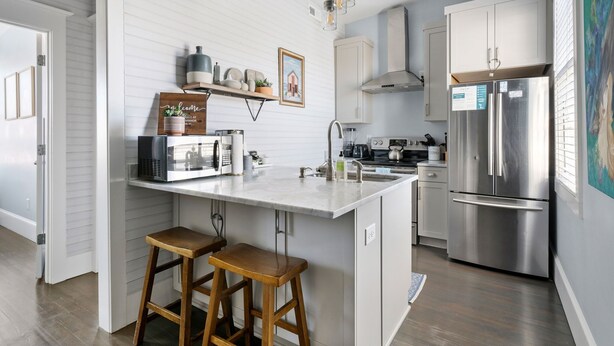 Une cuisine moderne dotée d’un îlot central, d’appareils électroménagers en acier inoxydable et de tabourets en bois.