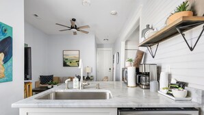 Une cuisine moderne avec un plan de travail blanc, des appareils en acier inoxydable et un ventilateur de plafond.