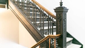 A staircase with ornate metal railings and a wooden handrail, leading to a landing with a decorative column. - Historic Studio w/ Lux Mattress Walk 2 Everything! (Spokane)