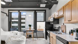 A compact studio apartment with a kitchenette, a dining area with a small table and chairs, and a bed with a white comforter. - Historic Studio w/ Lux Mattress Walk 2 Everything! (Spokane)