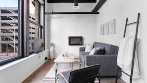 Un salon moderne avec un canapé gris, un fauteuil noir, une table basse en bois et un téléviseur fixé au mur.
