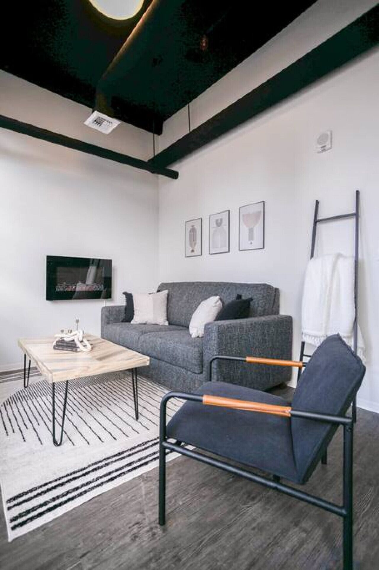 A modern, minimalist room with a grey sofa, a black chair, a wooden coffee table, and a flat-screen TV mounted on the wall.