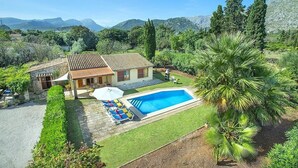 Une maison avec une piscine, entourée de verdure et de montagnes.