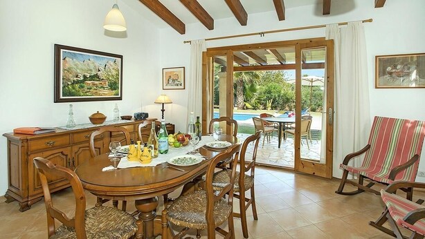 Un espace repas avec une table en bois, des chaises et une vue sur une piscine extérieure.