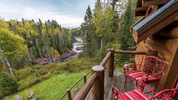 A wooden deck with red chairs and a view of a forest and river.