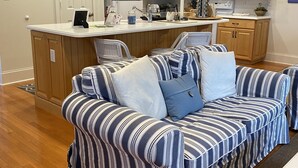 Una sala de estar acogedora con un sofá a rayas y una zona de cocina con armarios de madera y un refrigerador blanco.