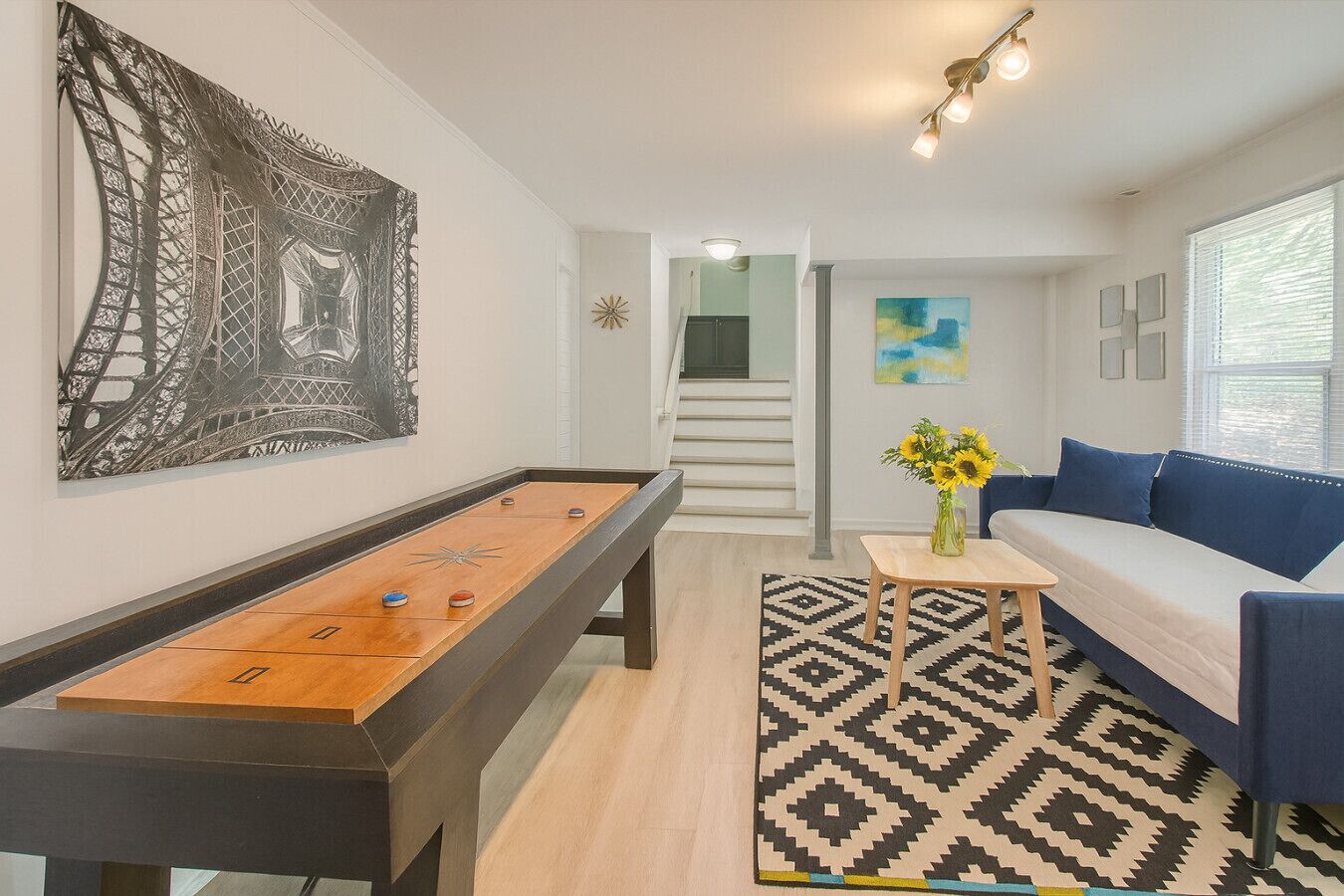 A room with a foosball table, a sofa, a patterned rug, and a painting of the Eiffel Tower.