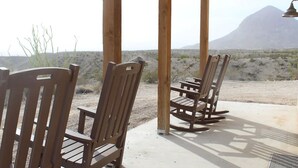 A wooden deck with chairs and a table, overlooking a desert landscape with sparse vegetation and a mountain in the distance. - Big Bend Lodging at Ten Bits Ranch | Room #8 - The Courthouse (Terlingua)