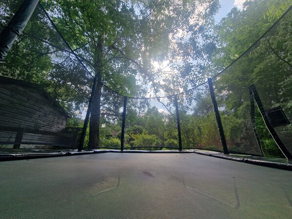 Un trampoline entouré d’arbres et délimité par une clôture en treillis métallique.