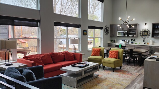 A spacious living room with a red sofa, a coffee table, and a dining area with chairs and a table. - Blue Haven Unit B All New - Downtown Moab! (Moab)