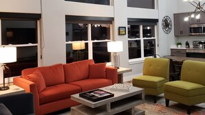 A modern living room with a red sofa, yellow armchairs, and a coffee table. There are large windows and a kitchen in the background. - Blue Haven Unit B All New - Downtown Moab! (Moab)