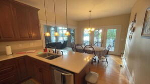 A kitchen with wooden cabinets, stainless steel appliances, a sink, and a dining area with a table and chairs. - Lazy Days Retreat (Hartfield)