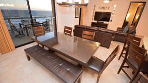 Ett rymligt vardagsrum med ett stort matbord, bekväma sittplatser, en tv och utsikt över havet.