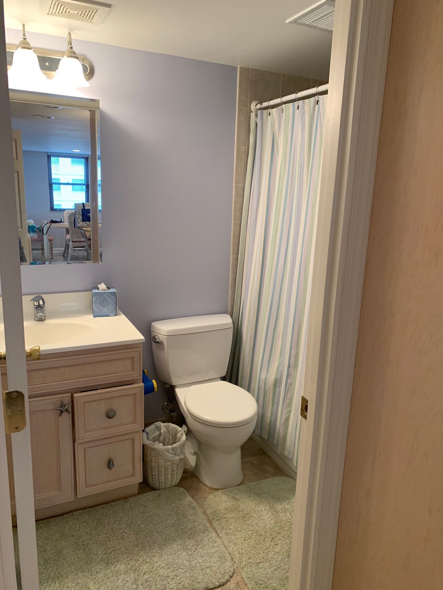 Une salle de bain avec des toilettes blanches, un lavabo avec un miroir et un rideau de douche.
