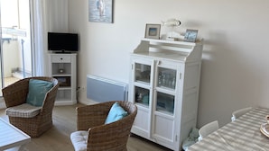 A living room with wicker furniture, a television, a cabinet with glass doors, and a checkered tablecloth. - Appartement Front de Mer Dans une Résidence de Prestige (NEUFCHATEL HARDELOT)