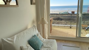 A living room with a white sofa, a small white table, and a view of the beach through large glass doors. - Appartement Front de Mer Dans une Résidence de Prestige (NEUFCHATEL HARDELOT)