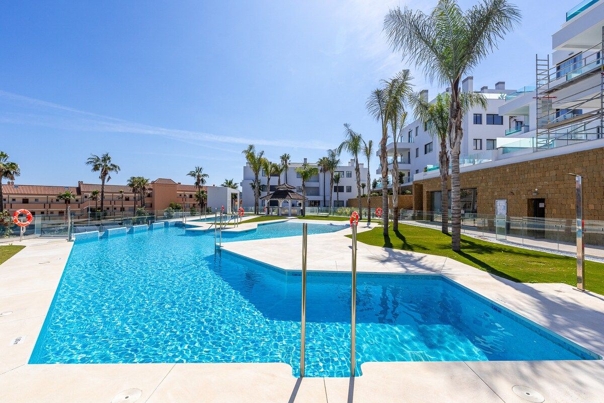 Piscina con múltiples carriles, rodeada de palmeras y edificios modernos.