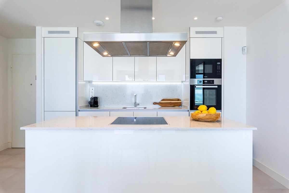 A modern kitchen with a central island, built-in appliances, and a stainless steel range hood.