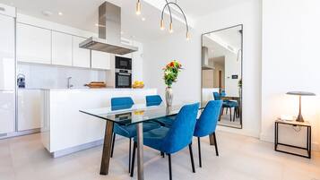Una cocina moderna con armarios blancos, una isla central con asientos y un comedor con sillas azules.