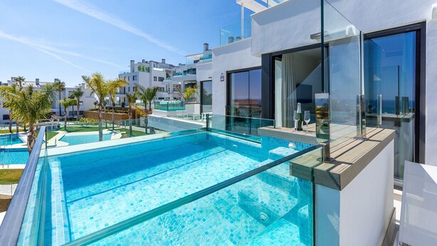 Ein moderner Poolbereich mit klarem, blauem Wasser, umgeben von Glasgeländern und einer Holzterrasse.