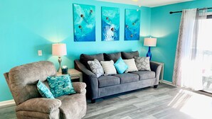 A living room with a grey sofa, a brown armchair, and teal artwork on the wall.