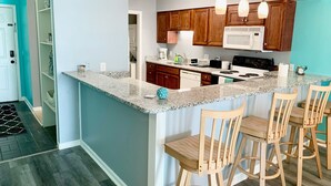 A modern kitchen with a granite countertop, wooden cabinets, a built-in oven, and a bar area with wooden stools.