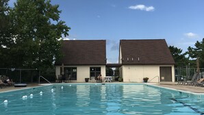 Una piscina con agua azul cristalina, rodeada de sillas de descanso y un edificio con techo marrón.