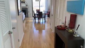 Un pasillo con piso de madera, puertas blancas, una zona de comedor con mesa y sillas, y una consola negra con objetos decorativos.