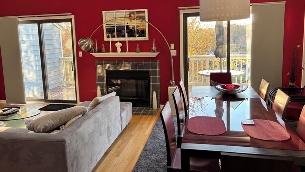 Una sala de estar con chimenea, una mesa de comedor con sillas, un sofá y un ventanal con vistas a árboles.