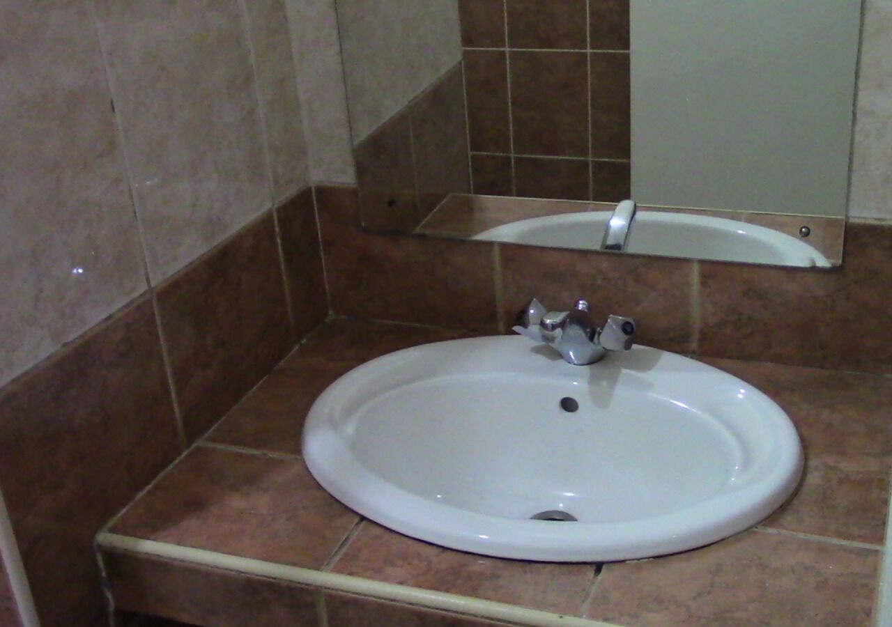 A bathroom with a white sink, a mirror above it, and brown tiled walls.