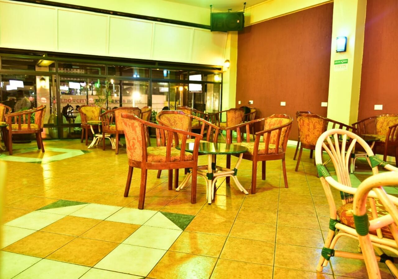 A lobby with a tiled floor, wooden chairs, and a glass partition.