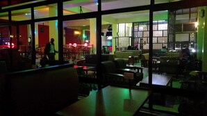 A dimly lit restaurant with large windows, tables, and chairs arranged for dining. - Klique Hotel (Eldoret)