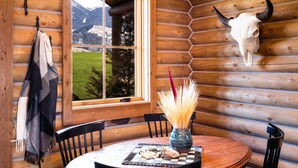 Un intérieur en bois avec une table ronde, des chaises, une fenêtre donnant sur les montagnes et un crâne de vache accroché au mur.