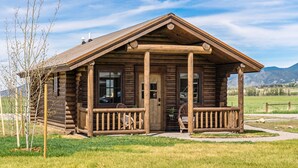 Une cabane en rondins avec une véranda et un petit jardin.