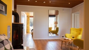 Een moderne woonkamer met een open haard, een gele fauteuil en een ronde salontafel met een boek en wijnglazen.