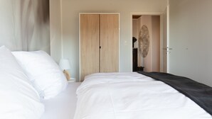 Een slaapkamer met een bed, een kledingkast en een deur naar een andere kamer.