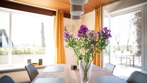 Een vergaderruimte met een houten tafel, zwarte stoelen, een vaas met paarse bloemen en een raam met gordijnen.