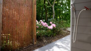 Een houten omheining, een tuin met roze bloemen en een witte buitenmuur met een tuinslang.